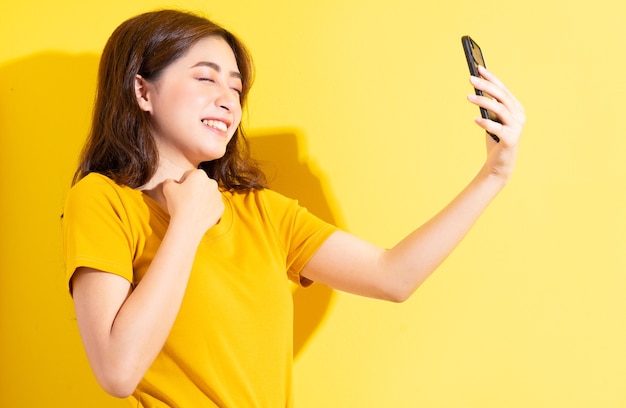 Smartphone di uisng giovane ragazza asiatica su colore giallo