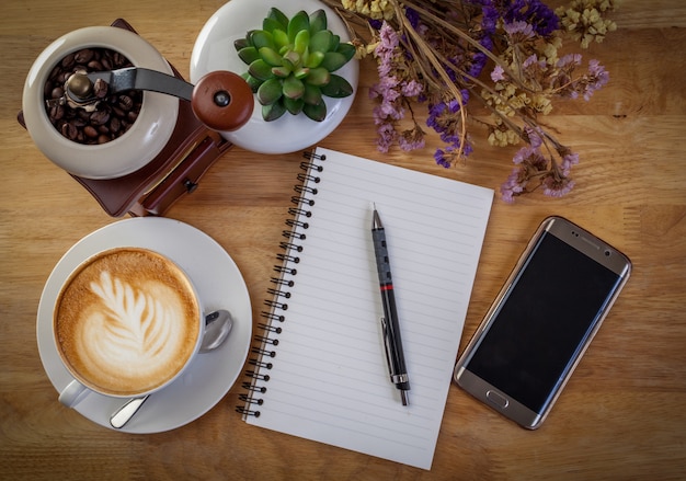 Smartphone, diario, fiore e tazza da caffè sul tavolo di legno.