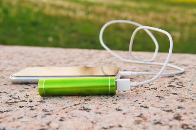 Smartphone e power bank esterno giacciono sulla superficie di granito del parco durante la ricarica