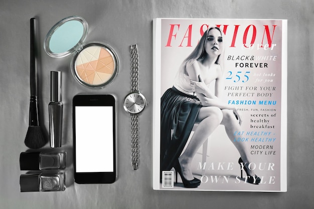 Smartphone e rivista dell'orologio da polso dei cosmetici sulla vista superiore del fondo grigio