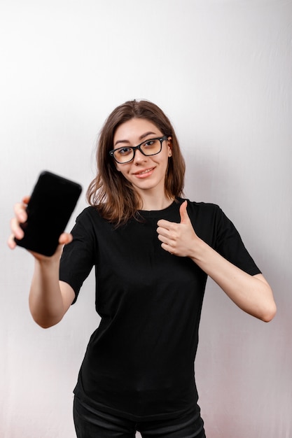 Smartphone europeo stupefacente e sveglio della tenuta della donna nella mano destra mentre sorridendo, facendo pubblicità