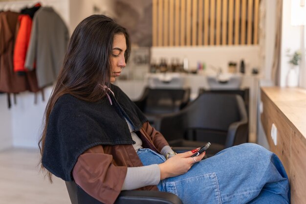 Smartphone focalizzato di navigazione della donna nel salone di parrucchiere