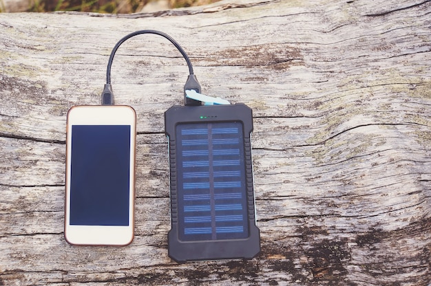 Smartphone in carica con power bank rosa con batteria solare su sfondo di legno, messa a fuoco selettiva e soft focus