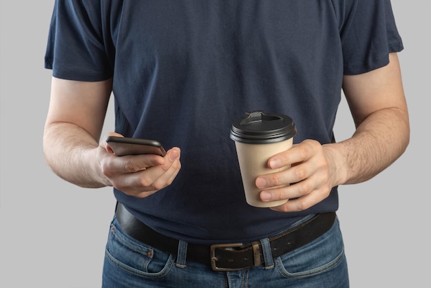Smartphone in mani maschili primo pianoUn uomo europeo con un telefono e un caffè in mano su uno sfondo grigio isolato