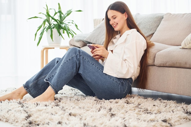 Smartphone in mano Giovane donna in camicia bianca e jeans è a casa