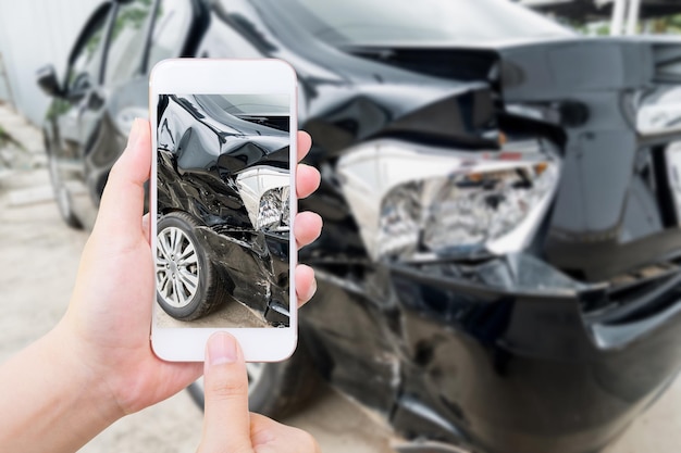 Smartphone mobile della tenuta femminile che fotografa l'incidente d'auto per l'assicurazione