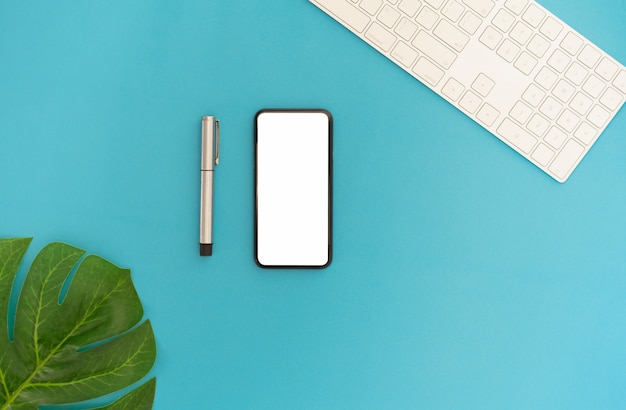 Smartphone moderno vista dall'alto e tastiera con foglie su sfondo di colore blu.