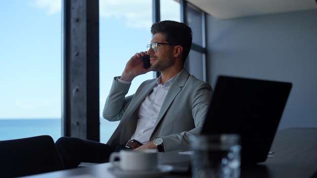 Smartphone parlante professionale positivo al posto di lavoro con vista sul mare Chiamata del direttore