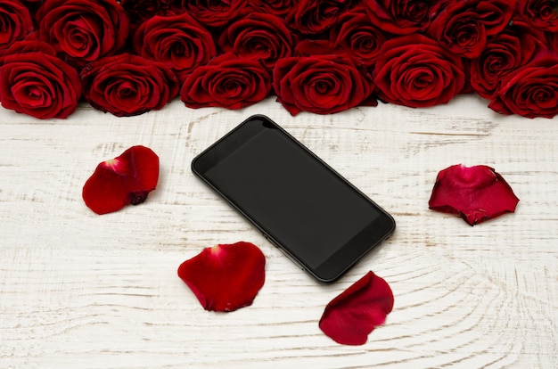 Smartphone riposa il tavolo di legno bianco sulla superficie dei petali e un mazzo di rose