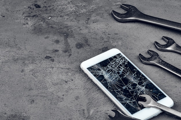 Smartphone schiantato con strumenti di riparazione su grigio