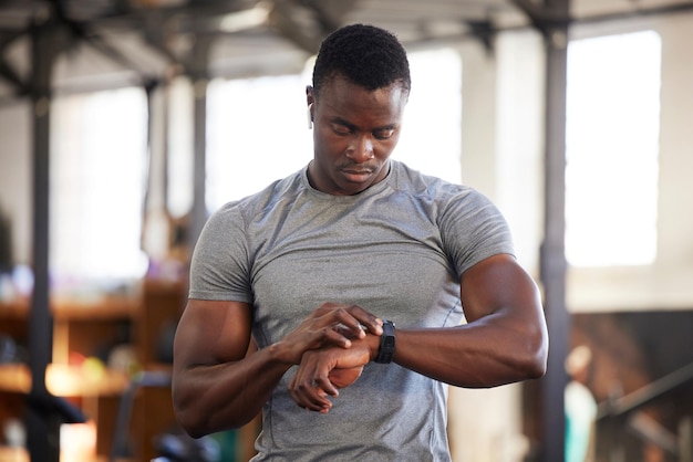 Smartwatch fitness e uomo di colore in palestra per l'allenamento o il monitoraggio dei risultati dell'esercizio o l'aggiornamento dei progressi Controlla il timer e la tecnologia dell'atleta bodybuilder o dello sportivo in salute e benessere