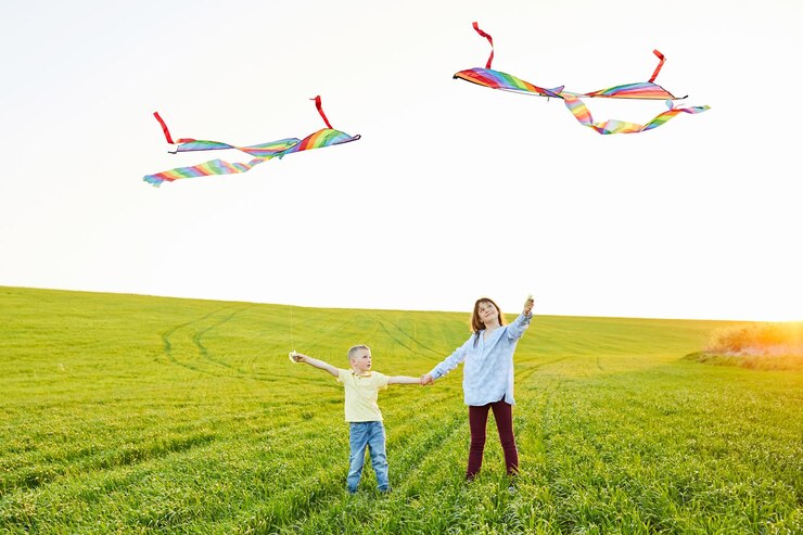 Smiling girl and brother boy standing and holding hands with flying colorful kites on the high grass meadow Happy childhood moments