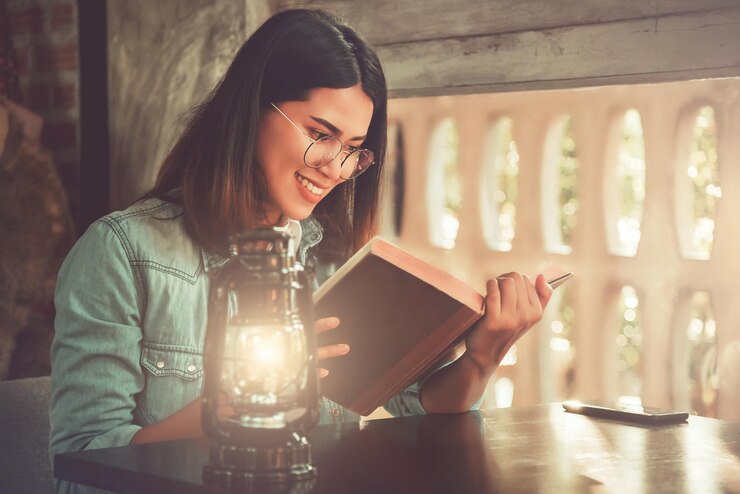 Photo smiling young woman reading book while sitting by table