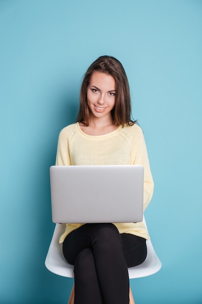 Smilling giovane donna che utilizza computer pc portatile isolato su sfondo blu