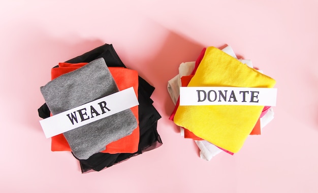 Smistamento dei vestiti nell'armadio di casa per la donazione e indossato con note di carta su sfondo rosa tenue.