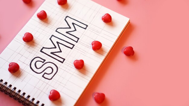 SMM Social media marketing testo su notebook su sfondo rosa con caramelle a forma di cuori