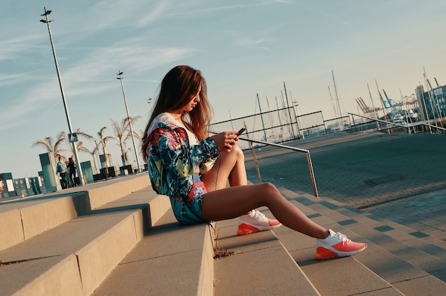 SMS ad un amico. Attraente giovane donna in abbigliamento sportivo utilizzando smart phone mentre è seduto sui gradini all'aperto