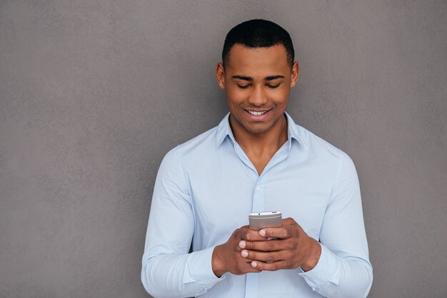 SMS ad un amico. Fiducioso giovane africano guardando il suo smartphone e sorridendo