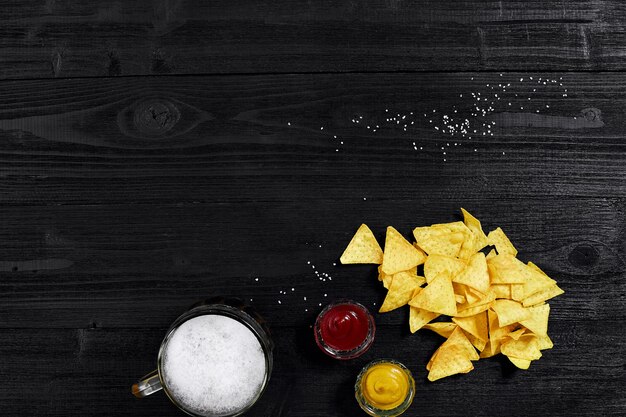 Snack per party chips nachos con salse ketchup mostarda e boccale di birra su sfondo nero...