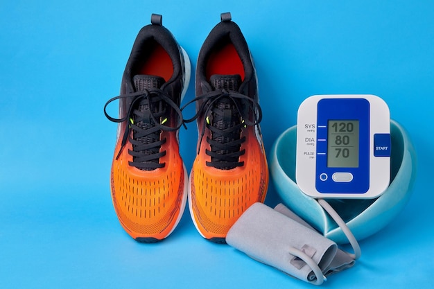 Sneakers arancioni e monitor per la pressione sanguigna in una ciotola a forma di cuore su sfondo blu