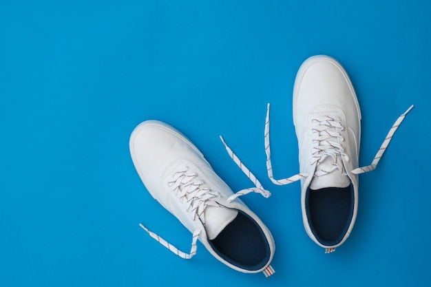 Sneakers bianche con lacci sciolti su superficie blu