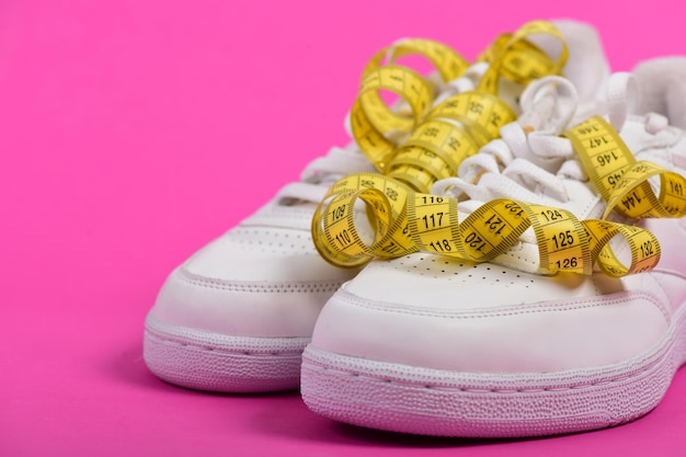 Sneakers con nastro di misurazione su sfondo rosa