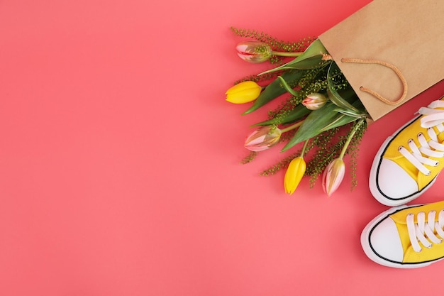 Sneakers e sacchetto di carta con fiori su sfondo rosa