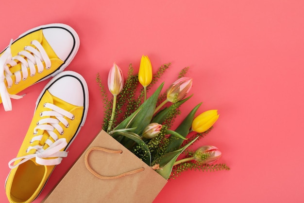 Sneakers e sacchetto di carta con fiori su sfondo rosa