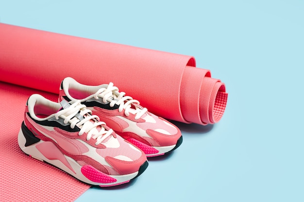 Sneakers rosa con tappetino da yoga su sfondo blu. Uno stile di vita sano. Allenamento a casa. Concetto di fitness moda minimalista.