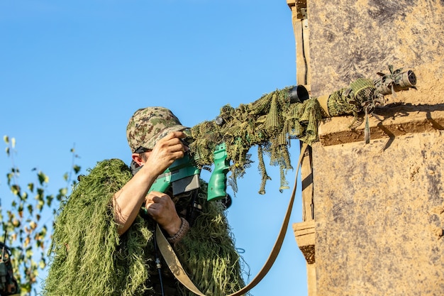 Sniper armato di grosso calibro, fucile da cecchino, sparando a bersagli nemici a distanza dal rifugio, seduto in agguato.