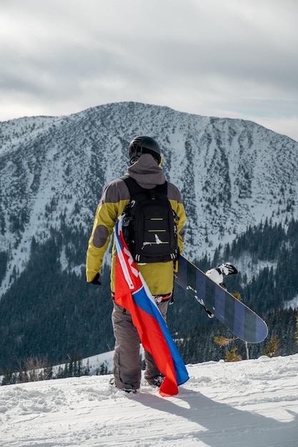 Snowboarder dell'uomo con la bandiera della slovacchia al pendio della stazione sciistica belle montagne del paesaggio sullo sfondo