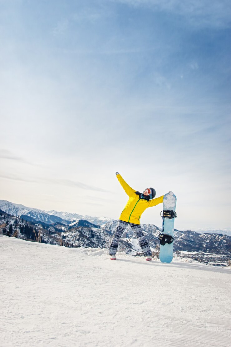 Snowboarder di giovane donna in giacca gialla e casco nero sullo sfondo di montagne innevate