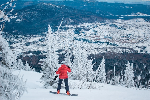 Snowboarder donna in giacca rossa e casco bianco scende dalla cima della montagna di neve sullo snowboard. Incredibile paesaggio invernale