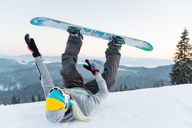 snowboarder femminile divertirsi sul pendio sdraiato sulla neve con le gambe in aria