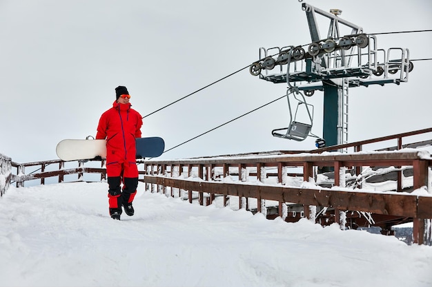 Snowboarder maschio in un abito rosso che cammina sulla collina innevata con il concetto di snowboard, sci e snowboard.