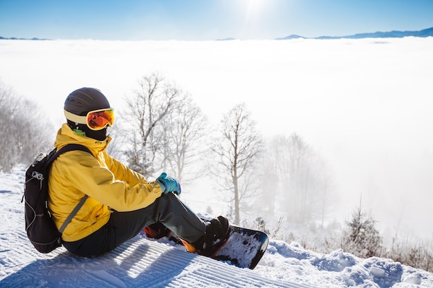 Snowboarder seduto e guardando la catena della montagna in background