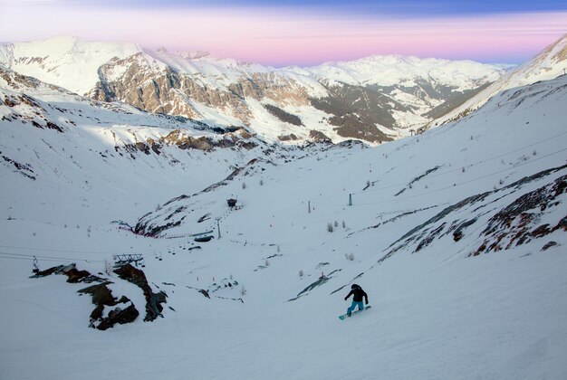 Snowboarder su una stazione sciistica invernale di fronte a montagne coperte di neve sotto un dolce cielo rosa