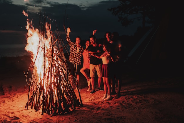 Società di svago di festa che si scalda intorno al falò sulla spiaggia.