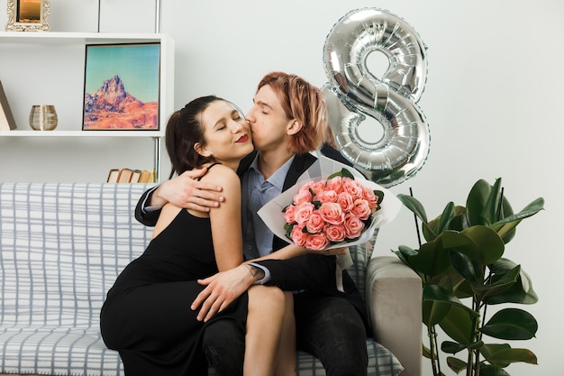 Soddisfatto degli occhi chiusi, si abbracciarono giovani coppie durante la felice giornata delle donne con un bouquet seduto sul divano nel soggiorno
