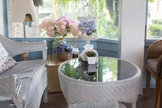 Sofà blu del rattan con il cuscino in salone accanto alla finestra con la vista del giardino in casa moderna.