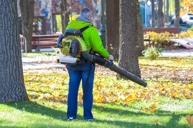 Soffiatore per foglie Il lavoratore maschio rimuove le foglie prato del giardino in autunno Rimozione delle foglie cadute in autunno Servizio di pulizia del parco