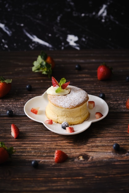 Soffici frittelle di soufflé con crema e frutti di bosco sul piatto bianco impostato sulla tavola di legno.