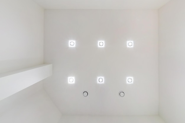 Soffitto sospeso con lampade alogene e costruzione in cartongesso in una stanza vuota in appartamento o casa Soffitto teso bianco e di forma complessa