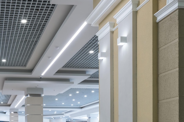 Soffitto sospeso e a griglia con lampade alogene e costruzione in cartongesso in una stanza vuota in un negozio o in una casa Soffitto teso bianco e di forma complessa