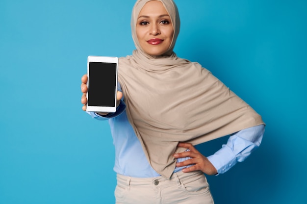 Soft focus sul telefono cellulare nelle mani della donna musulmana araba. Giovane donna in hijab che tiene uno smartphone e in posa