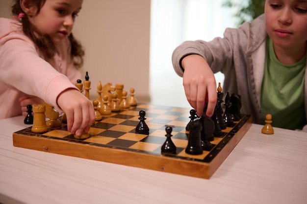 Soft focus sulle mani di un ragazzo felice e di una bambina che giocano a scacchi nell'interno della casa. Giochi da tavolo intellettuali intelligenti per bambini, sviluppo logico, concetto di educazione. Gioco di scacchi per una mente intelligente