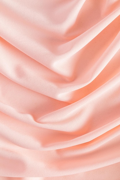 Soft pleats of peach colored satin textiles Luxury abstract textile background design Vertical view Colore dell'anno 2024 peachy fuzz