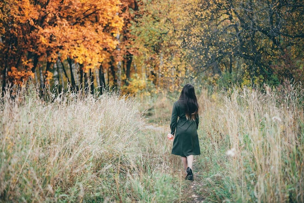 Sognante bella ragazza con lunghi capelli neri naturali su sfondo con foglie colorate.