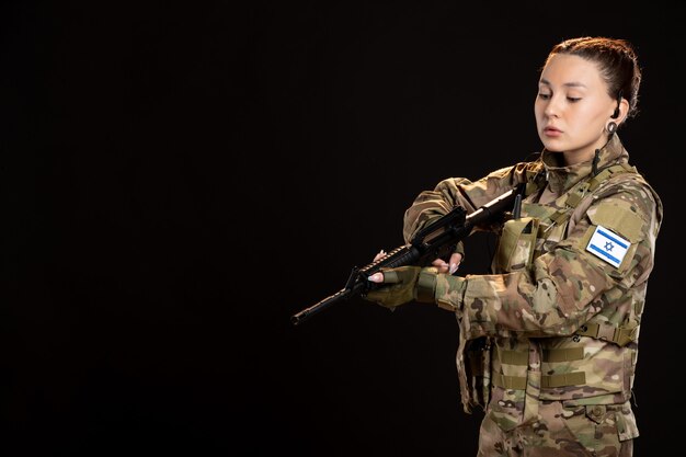 Soldato donna in mimetica che mira mitragliatrice sul muro scuro