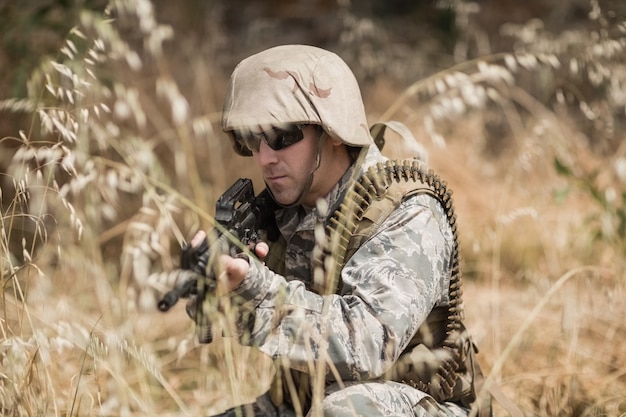 Soldato militare che si nasconde nell'erba mentre fa la guardia con un fucile nel campo di addestramento